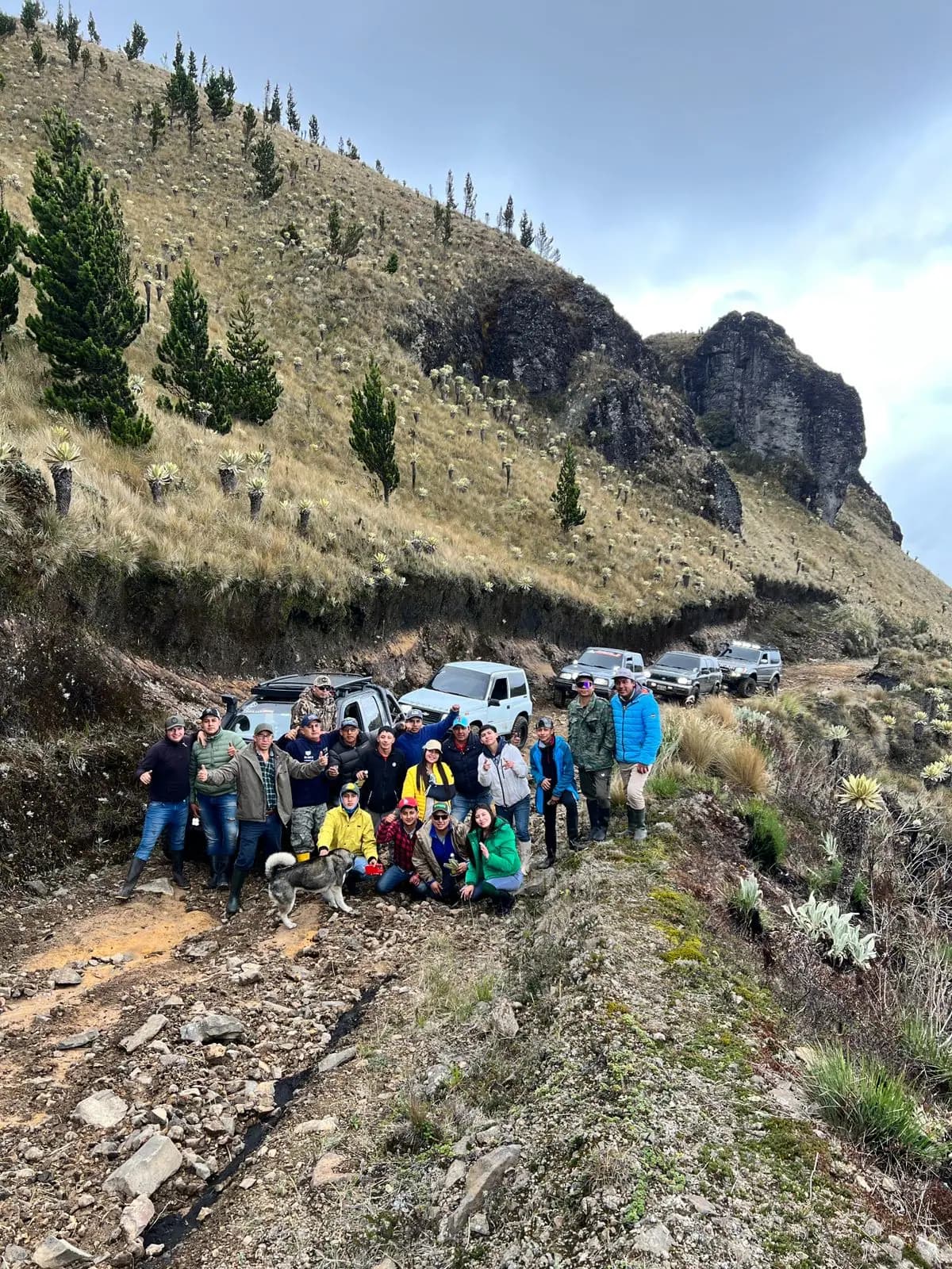El grupo completo posando junto a los 4x4 estacionados en el sendero, con el farallón de roca y los frailejones de la ladera al fondo
