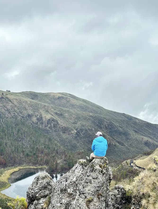 Un participante sentado en el peñasco mirando la laguna y las lomas del páramo