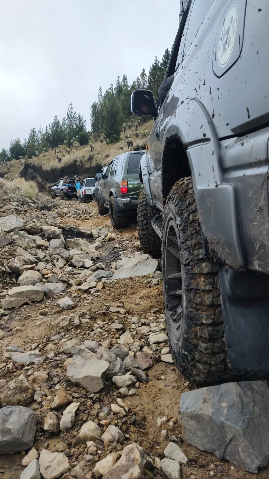 Primer plano de una llanta embarrada en el tramo de piedra, con el resto de la caravana adelante